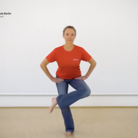 Eine Frau steht im Bewegungsraum der ASH Berlin, die Hände in den Hüften, ein Bein überkreuzt im stehen das andere