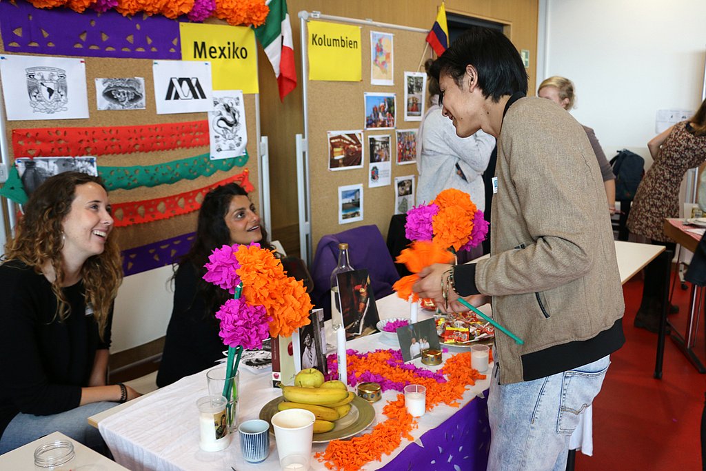 Ein Stand beim International Day- ein Besucher unterhält sich mit zwei Studentinnen, welche am Stand sitzen.
