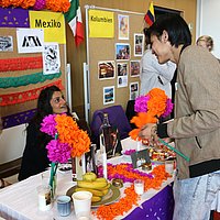 Ein Stand beim International Day- ein Besucher unterhält sich mit zwei Studentinnen, welche am Stand sitzen.