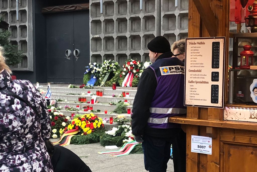 Vergrößern: Ein Mann mit einer Weste von PSNVNET steht vor der Treppe der Gedächtniskirche mit Kerzen auf dem Boden